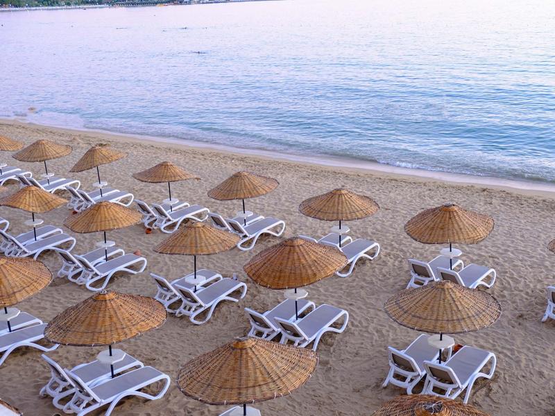 Prázdná lehátka se slámovými slunečníky na klidné písečné pláži u moře.