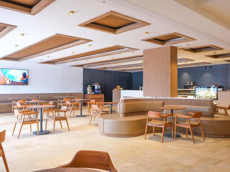 Světlá, moderní hotelová jídelna s dřevěným nábytkem a centrálním posezením.