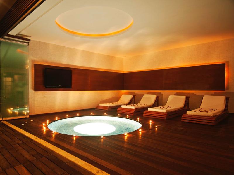 Relaxace místnost s osvětlenou vířivkou a lehátky obklopenými svíčkami.