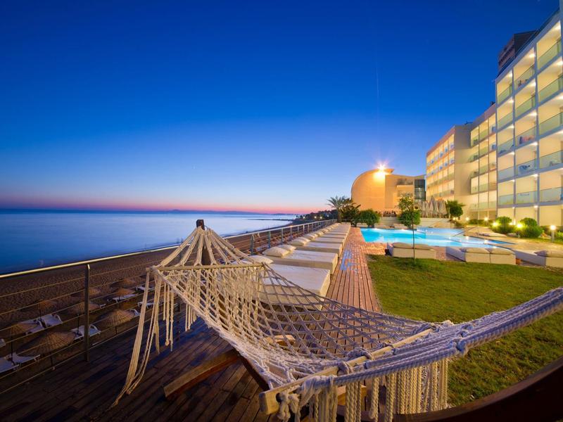 Houpací síť na dřevěné terase u hotelového bazénu s výhledem na moře za západu slunce.