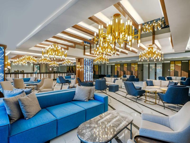 Spacious hotel lobby with blue and gray seating, gold chandeliers, and modern decor.
