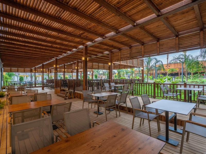 Spacious outdoor patio with wooden roof, tables, and chairs overlooking green garden.