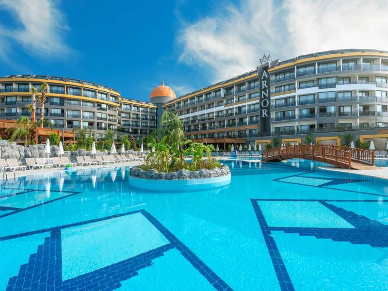 Luxury hotel with large outdoor pool and modern curved architecture under blue sky.