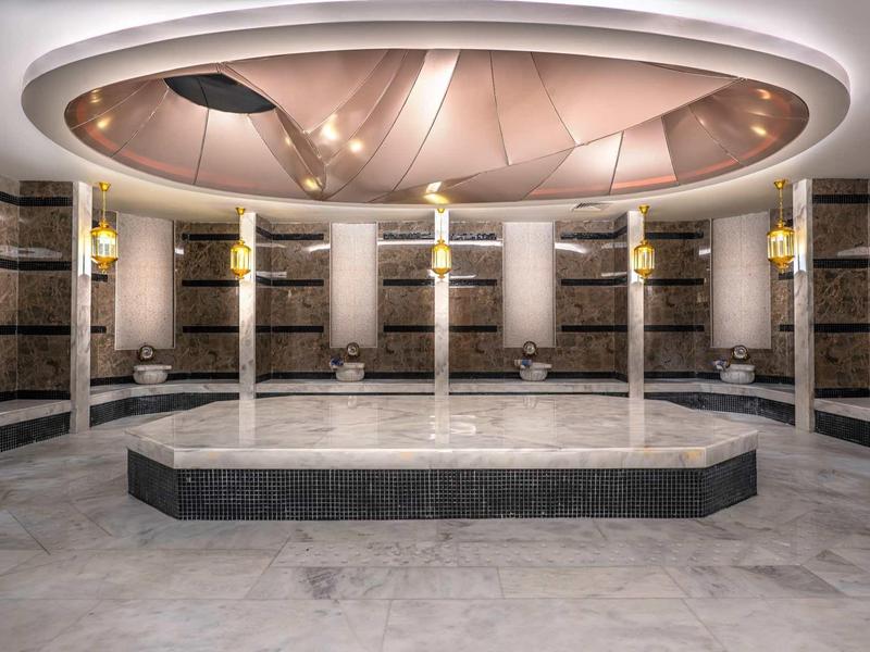 Luxurious marble spa room with pillars and central hexagonal water feature under soft lighting.