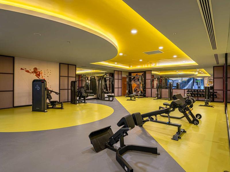 Modern indoor gym with yellow curved ceiling lights and black exercise equipment.