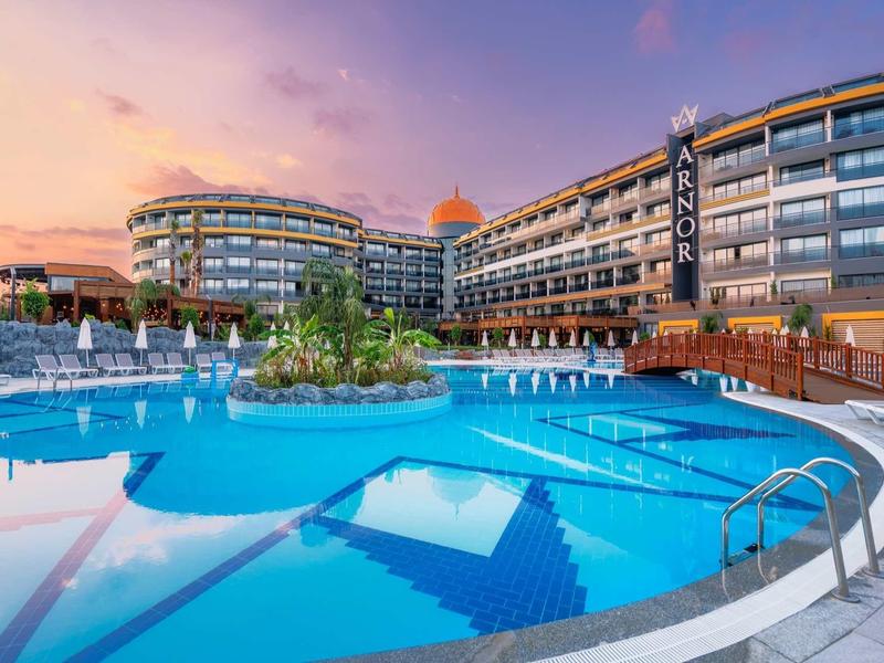 Modern hotel with large outdoor pool and sun loungers at sunset.