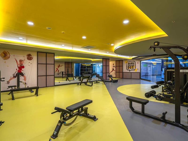 Modern gym with yellow and gray floor, workout benches, and ceiling lights.