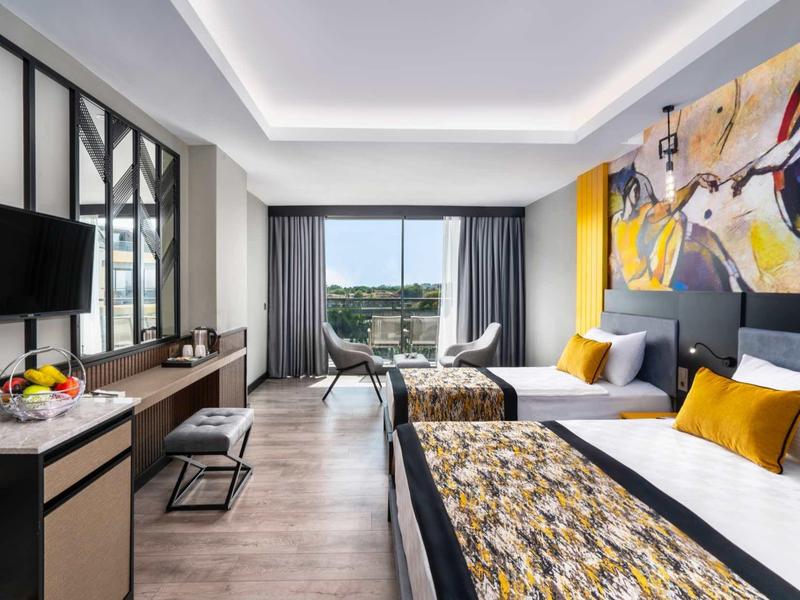 Modern hotel room with twin beds, colorful artwork, and a city view from the window.