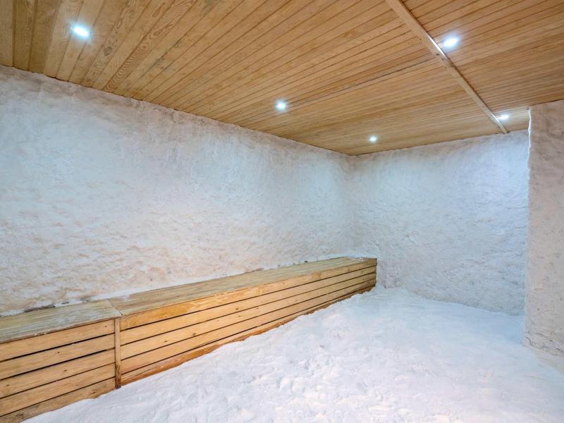 Sauna room with wooden bench, white stone walls, and wooden ceiling with recessed lights.