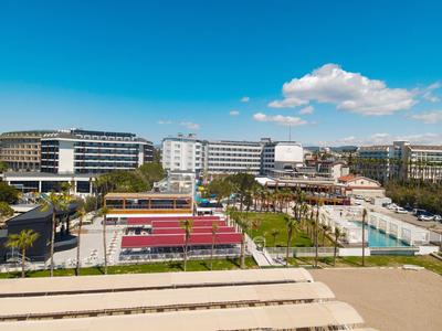 Modern stadsplein met tennisbanen, wandelpaden en omliggende gebouwen onder een blauwe lucht.