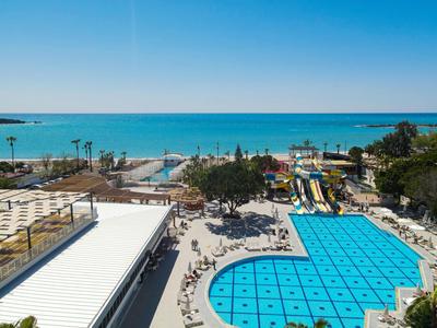 Buitenzwembad met glijbanen en zeezicht onder heldere blauwe lucht
