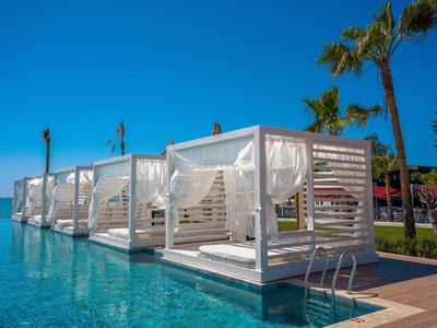 Piscina con modernas cabañas blancas y palmeras bajo un cielo despejado.