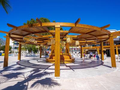 Houten ronde pergola met mensen die ernaast lopen onder een heldere blauwe lucht.