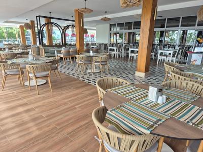 Modern restaurant met houten vloeren, ronde tafels en gestoffeerde stoelen in een lichte ruimte.