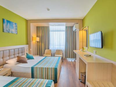 Lichte hotelkamer met twee bedden, groene muren, een tv en zitplaatsen bij het raam.