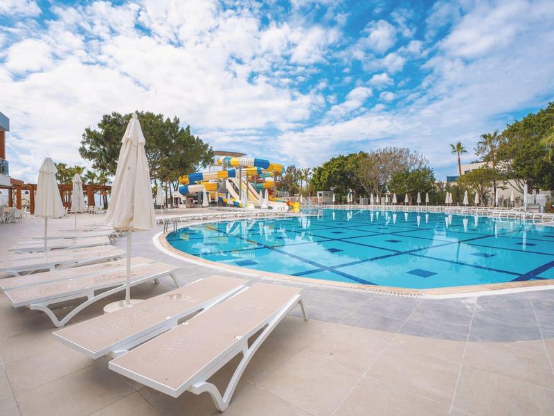 Rond hotelzwembad met ligstoelen en parasols onder blauwe lucht.