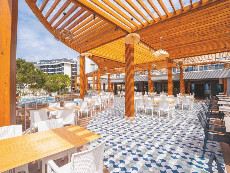 Groot buitenterras met houten dak en veel tafels en stoelen, lichte patroonvloer