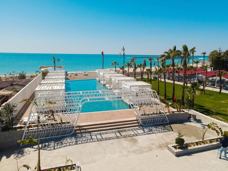 Strandresort met zwembaden, palmbomen en uitzicht op de oceaan onder een heldere blauwe lucht.