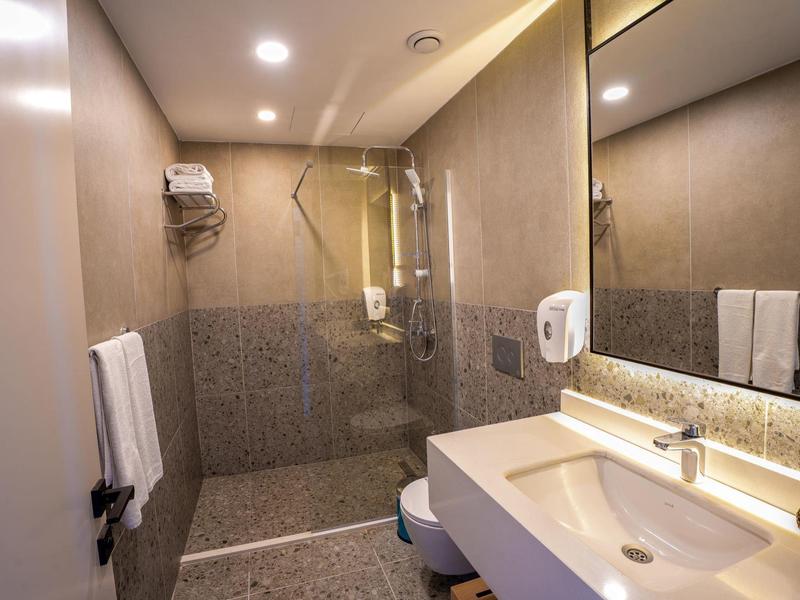 Moderne hotelbadkamer met inloopdouche, grote spiegel en witte wastafel.