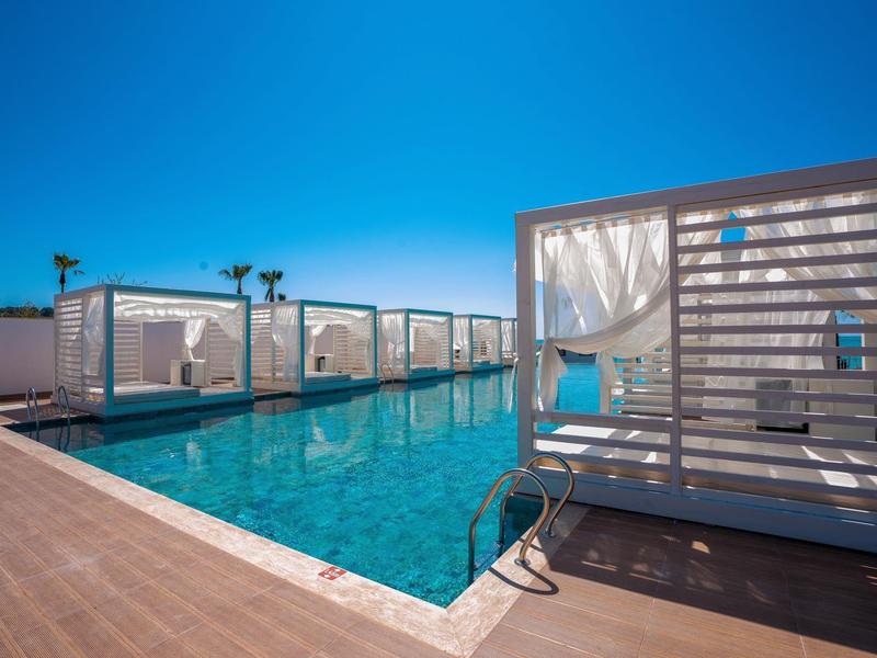 Buitenzwembad met cabana's onder een heldere blauwe lucht bij een hotel.