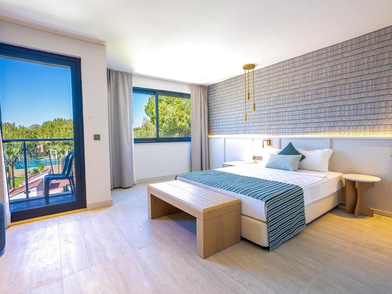 Lichte hotelkamer met kingsize bed, nachtlampjes, balkon en stadszicht met moderne inrichting.