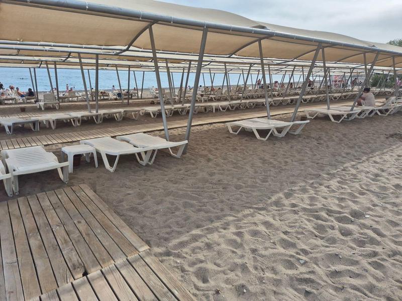 Lege ligstoelen onder schaduwstructuren op een zandstrand met houten loopbrug