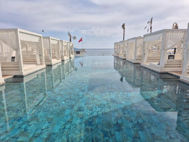 Infinity-zwembad met witte ligbedden en uitzicht op zee bij bewolkte lucht.