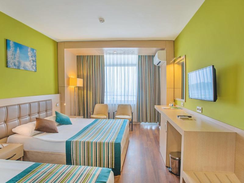 Lichte hotelkamer met twee bedden, groene muren, een tv en zitplaatsen bij het raam.