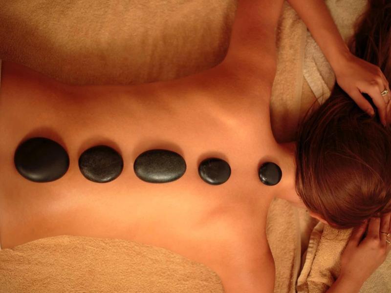 Osoba ležící s teplými kameny na zádech během masáže.