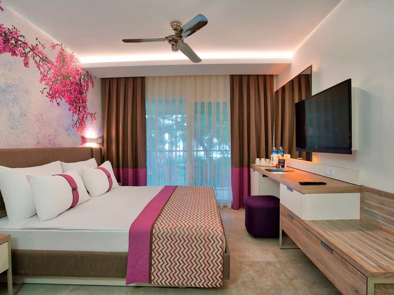 Moderní hotelový pokoj se dvoulůžkem, růžovou výzdobou, nástěnným uměním a velkým oknem s závěsy.