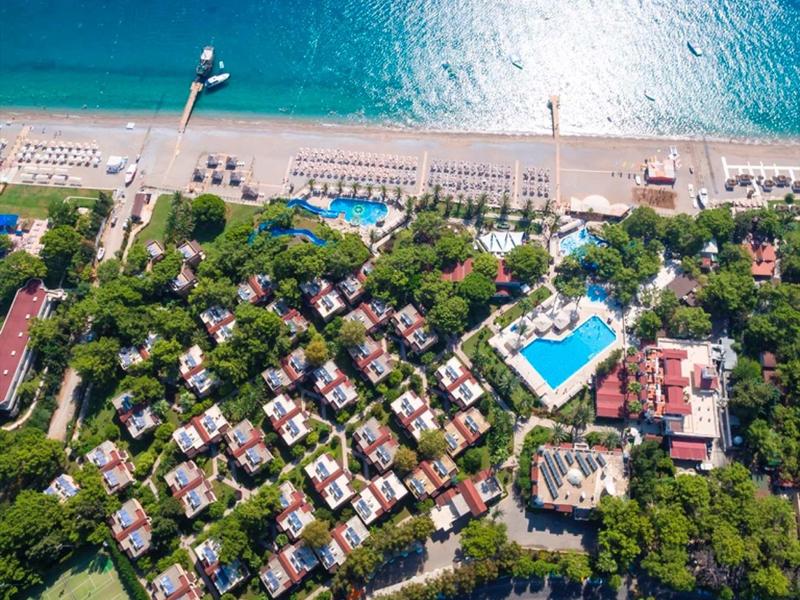 Letecký pohled na plážové letovisko s bazény, tenisovým kurtem a slunečníky podél pobřeží.
