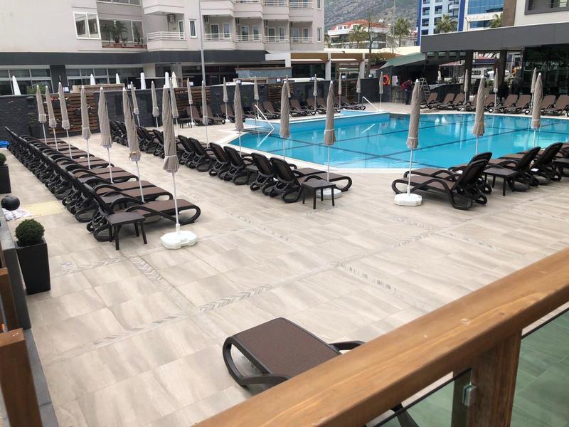 Moderne zwembadzone met vele ligstoelen en hoge parasols naast hotelgebouwen.