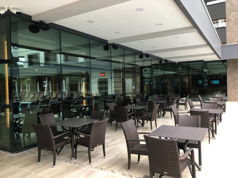 Buitenterras van een hotel met moderne glazen wanden en meerdere tafels en stoelen.