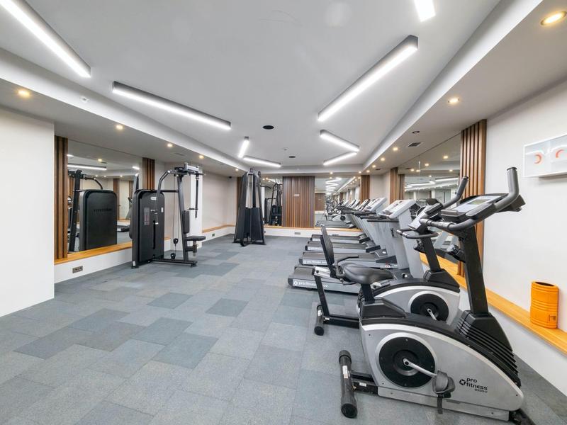 Moderne fitnessruimte met diverse trainingsapparaten en grijze tapijtvloer.