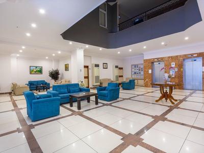 Geräumige Lobby mit weiß-kariertem Boden, blauen Sofas, Holztisch und hellen Deckenlampen.