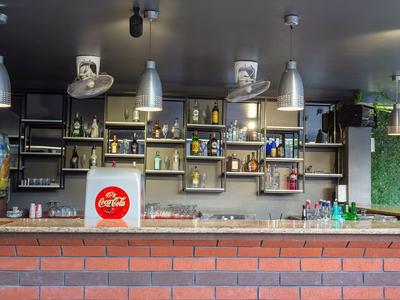 Moderne Bar mit roten Ziegeln, hängenden Lampen und Regalen voller Flaschen und Gläser.