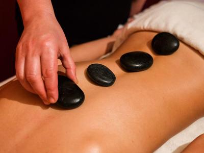 Drei schwarze heiße Steine werden auf dem nackten Rücken einer Person bei Massage gelegt.