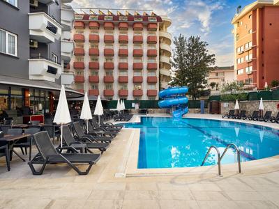 Basen hotelowy z niebieskimi zjeżdżalniami, leżakami i parasolami w miejskiej okolicy.