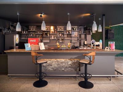 Espace bar d'hôtel moderne avec deux tabourets, étagères éclairées et décoration élégante.