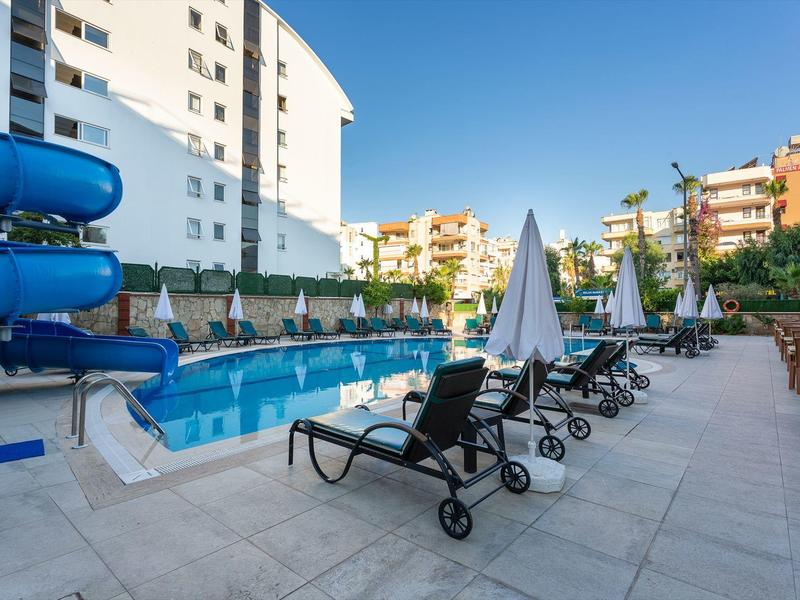 Espace piscine moderne avec toboggan aquatique, chaises longues et parasols dans un complexe hôtelier.