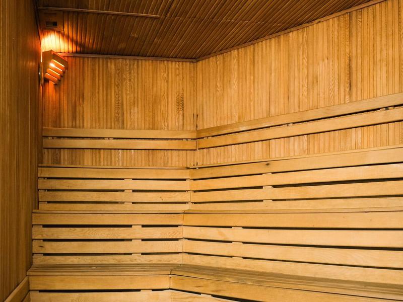 Sauna en bois clair avec larges bancs et lumière chaude au mur.