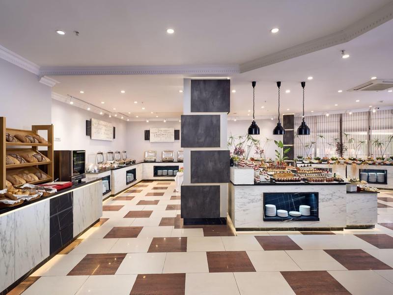 Buffet d'hôtel moderne et lumineux avec diverses stations de repas et grande présentation.