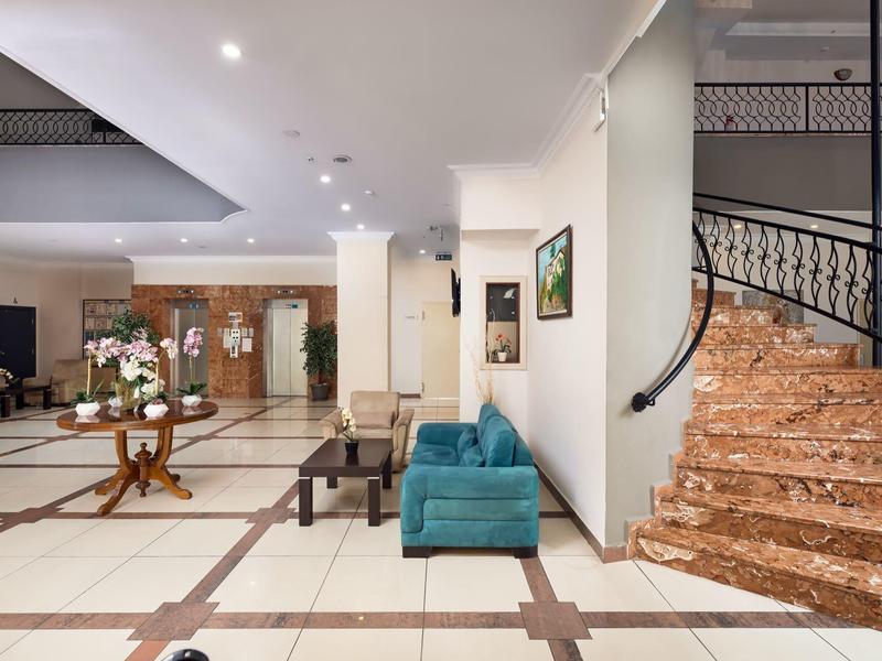 Hall d'hôtel lumineux avec escalier en marbre, canapé bleu et fleurs sur une table en bois.