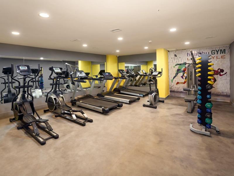 Salle de sport moderne avec tapis de course, vélos elliptiques et haltères dans une pièce lumineuse.