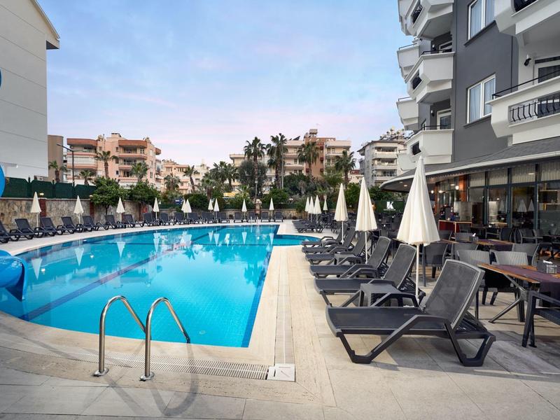 Piscine d'hôtel avec chaises longues bleues et parasols à côté de bâtiments modernes.