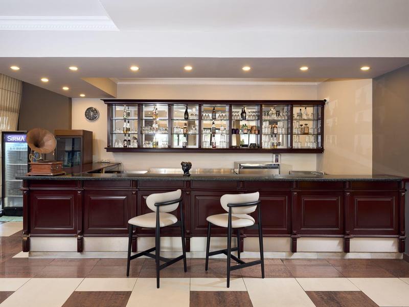 Bar d'hôtel élégante avec bois foncé et deux tabourets devant une étagère éclairée.