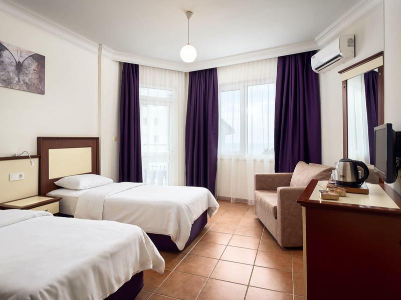 Chambre d'hôtel lumineuse avec deux lits simples, canapé et grandes fenêtres avec rideaux.