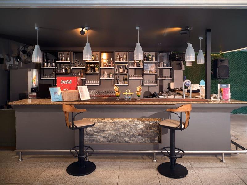 Espace bar d'hôtel moderne avec deux tabourets, étagères éclairées et décoration élégante.