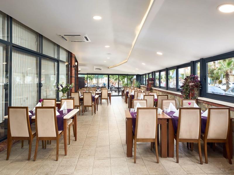 Grande salle à manger lumineuse avec tables, chaises et grandes fenêtres donnant sur la verdure.