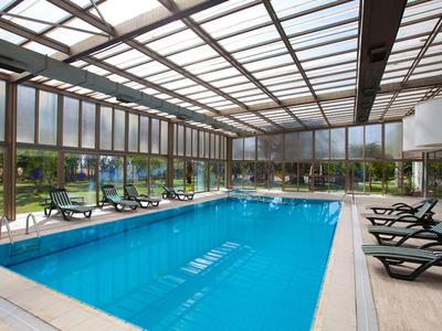 Piscine intérieure avec chaises longues et grandes fenêtres en verre donnant sur un jardin.